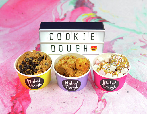 Three tubs of cookie dough in front of a Lightbox that says 'cookie dough', on a pink marble table